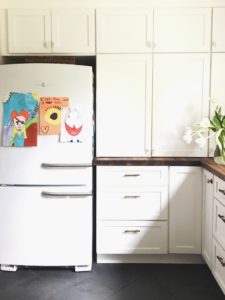 kid art on refrigerator, basket on top, white cabinets